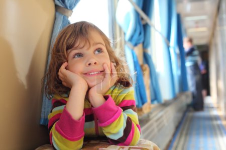 Girl sits in corridor of railway car and looks upward