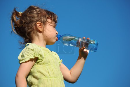 Girl drinks water from plastic bottle against blue sky