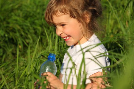 Smiling little girl in grass with plastic bottle