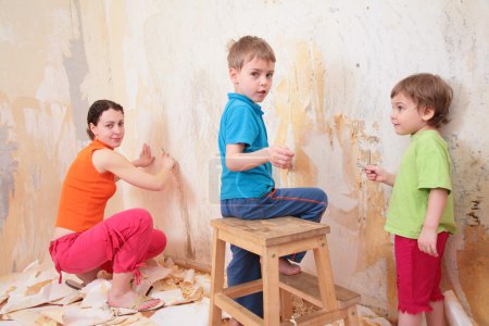 Children help mother remove old wallpapers from wall