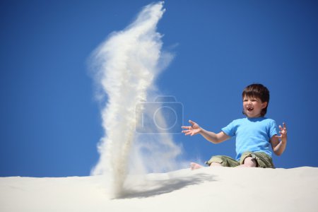 Boy sits on sand and scatters it