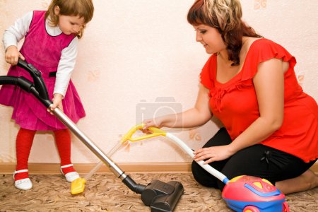 Little Girl and woman vacuum a carpet