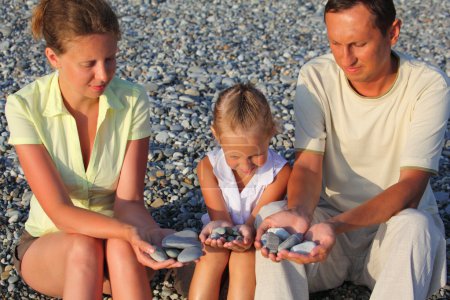 Parents and daughter sits in pebbly beach