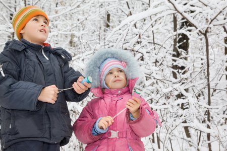 Cheerful boy and little girl with petard in hands in winter in w