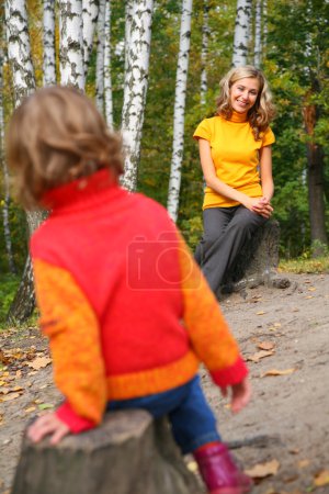 Mother with child sit on stubs in wood in autumn