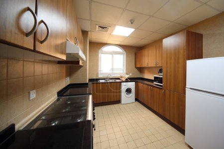 Kitchen with brown cupboards, washingmachine, cooker and fridge