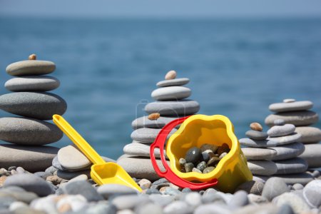 Yellow children's bucket with scoop and stone stacks on seacoas