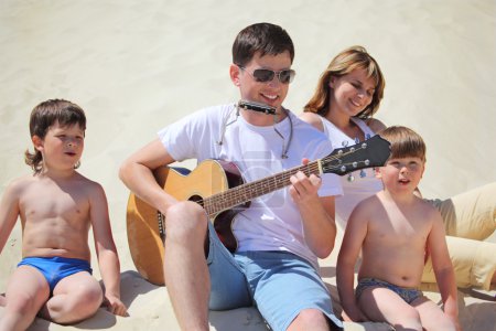 Guy in sunglasses plays guitar and lip accordion with children