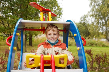 Boy in jacket is on playground in autumn park
