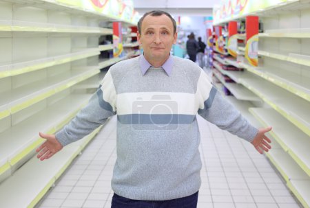 Elderly man stands between empty shelves in shop with dissolved