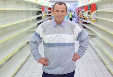 Elderly man stands between empty shelves in shop