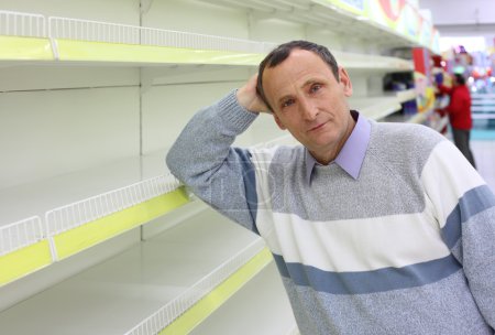 Elderly man leans against empty shelves in shop