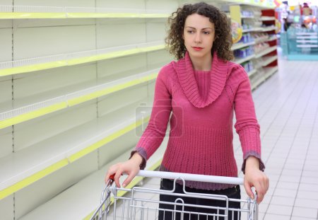 Young woman with cart in shop with empty shelves