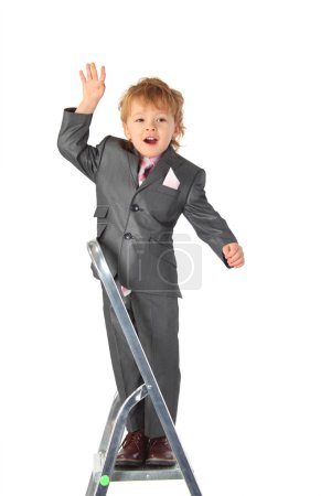 Boy in suit balances at step-ladder top