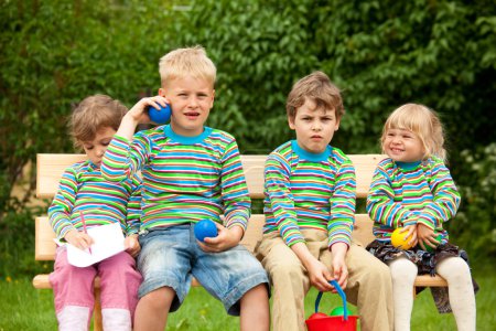Two boys and two girls on a bench in park. In identical stripe c