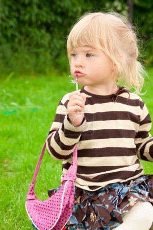 The little girl paints lips in park
