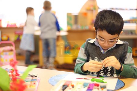 Boy in glasses moulds from plasticine on table in kindergarten