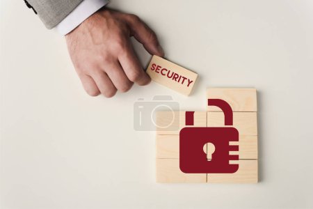 partial view of man holding brick with 'security' lettering over wooden blocks with lock icon isolated on white