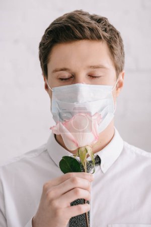 man with pollen allergy in medical mask smelling rose with closed eyes