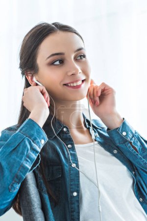 beautiful smiling teenage girl listening music in earphones and looking away