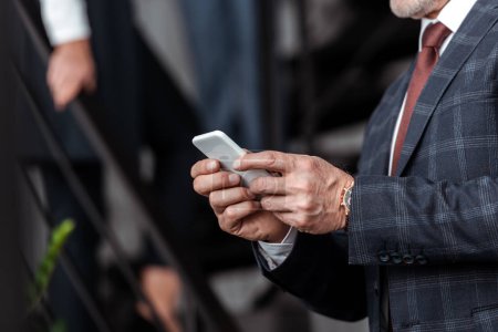cropped view of businessman using smartphone in office 