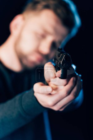 selective focus of criminal aiming gun at camera isolated on black