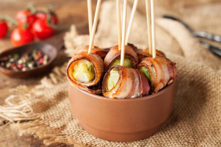 Bacon wrapped brussels sprouts served with cherry tomatoes in ceramic bowl. Appetizer rolls