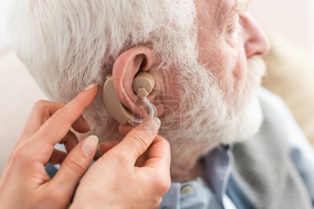 Cropped view of woman helping grey haired man, wearing hearing aid