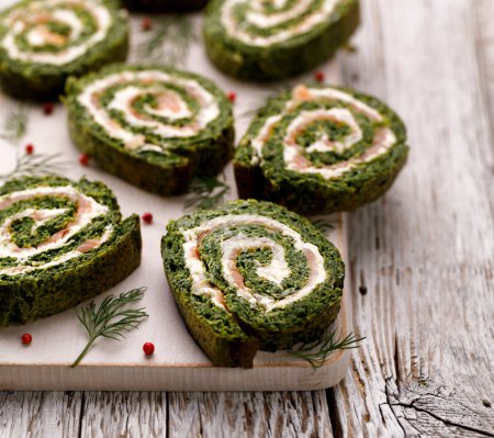 Spinach roulade stuffed with cream cheese and smoked salmon sliced on a white board, close-up.  Delicious appetizer, party food