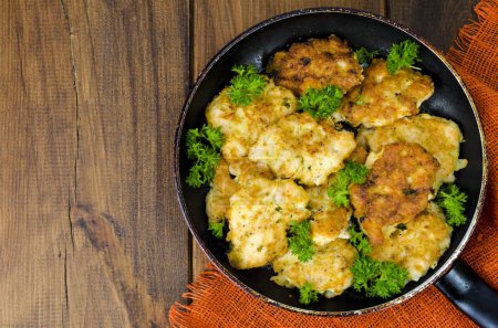 Fried meat pancakes in pan, vegetables, wooden background
