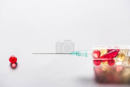 close up of syringe with medication near red round pill on grey background 