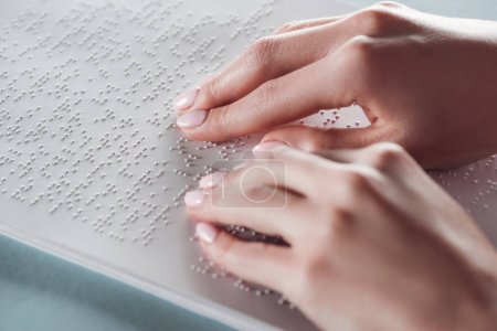 cropped view of girl reading braille text with hands on white paper
