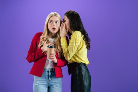 Brunette girl wishpering secret in friend's ear on purple background