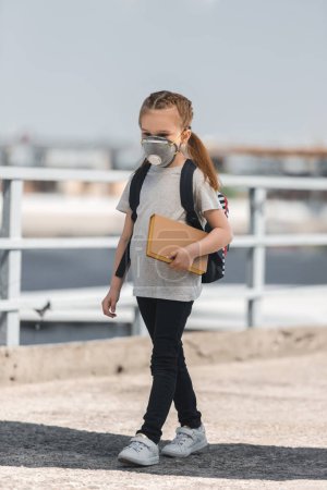 child in protective mask walking with book on bridge, air pollution concept