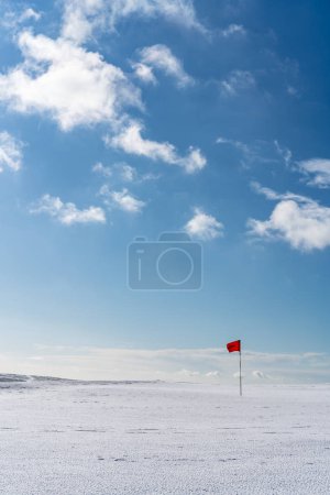 Snow covered deserted golf green with red flag, on Cleeve Hill, 