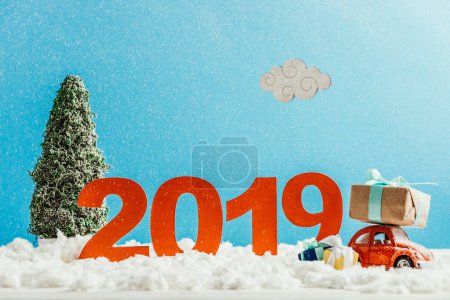 big red 2019 numbers with toy car, gifts and christmas tree on snow for new year