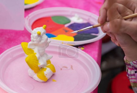 Child paints a ceramic figurine with bright colors. Ceramic staruette for coloring.
