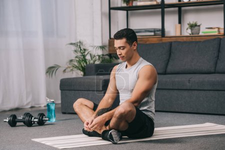handsome bi-racial man sitting on fitness mat with closed eyes