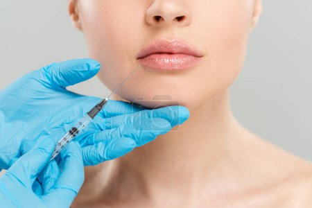 cropped view of cosmetologist holding syringe near face of woman isolated on grey 