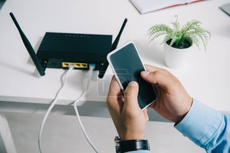 cropped view of businessman holding smartphone near plugged router