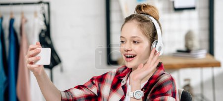 Panorama shot of teenager in headphones waving hand during video call