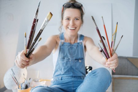 Female artist hand painter with brushes in front of the canvas and drawing. Artist studio interior. Process in art workshop.