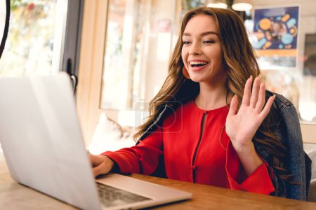 cheerful blogger waving hand while having video call on laptop 