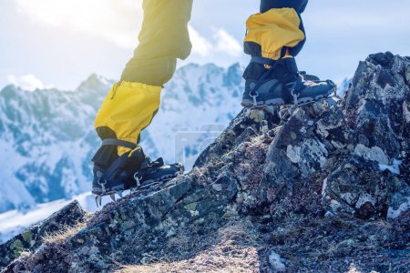 Climber in crampons stands on the rocks in front of the entrance to the peak on the background of the snowy mountains. Feet close up. The concept of the travel path and achieving the goal