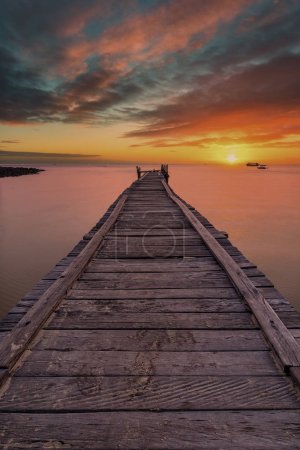 Old wooden pier stretching out into the sea with a dramatic sunset.