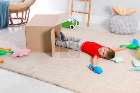 Cute little boy playing with cardboard box at home