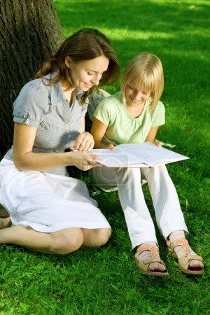 Mother And Daughter Reading The Book In A Park. Education Concep