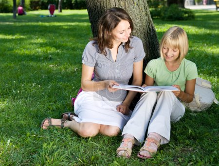 Mother And Daughter Reading The Book In A Park. Education Concep