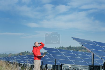 Engineer using laptop at solar panels plant field