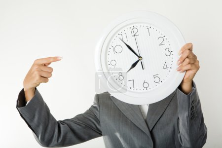 Image of female's hands holding clock in front of face and pointing at it